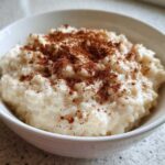 Close-up of a white bowl filled with creamy rice pudding generously sprinkled with ground cinnamon.