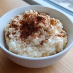 A close-up of a white bowl filled with creamy rice pudding recipe, generously dusted with ground cinnamon.