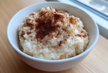 A close-up of a white bowl filled with creamy rice pudding recipe, generously dusted with ground cinnamon.