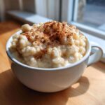 A close-up of creamy rice pudding recipe served in a white mug, generously dusted with cinnamon.