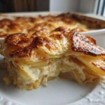 A thick slice of creamy scalloped potatoes recipe with a golden brown, cheesy top, served on a white plate.