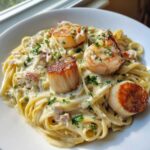 Close-up of creamy seafood pasta topped with seared scallops, shrimp, and crab meat.