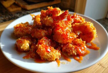 A plate piled high with crispy, golden brown bang bang shrimp drizzled generously with a bright orange spicy sauce.