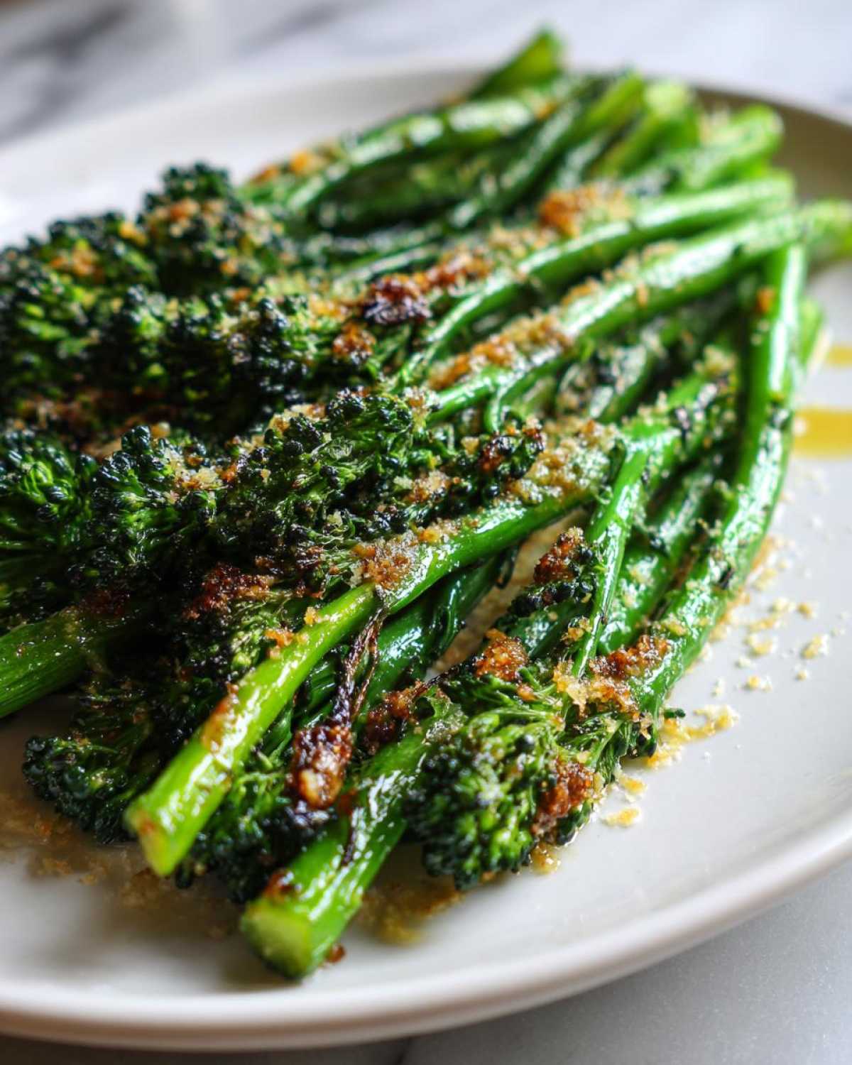 Close-up of bright green, cooked broccolini spears topped with toasted breadcrumbs and seasoning.
