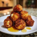 A stack of crispy, golden brown goat cheese balls being drizzled with honey on a white plate.