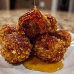 Close-up of crispy, golden brown goat cheese balls being drizzled with thick honey on a white plate.