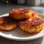 Four golden-brown, crispy mashed potato cakes stacked slightly on a white plate, ready to eat.