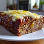 A thick slice of moist crockpot french onion meatloaf topped with melted white cheese and a savory glaze.