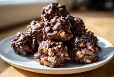 A pile of freshly made crockpot peanut clusters coated in rich chocolate, sitting on a white plate.