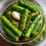 Overhead close-up of bright green dilly beans packed tightly in a glass jar with brine, dill, garlic, and pickling spices.