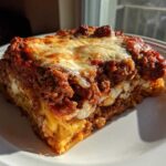 A thick, golden slice of baked spaghetti pie topped with rich meat sauce and melted mozzarella cheese.