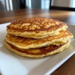 A stack of three perfectly golden brown, fluffy almond flour pancakes on a white rectangular plate.