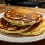 A stack of three fluffy almond flour pancakes drizzled with syrup on a white plate.