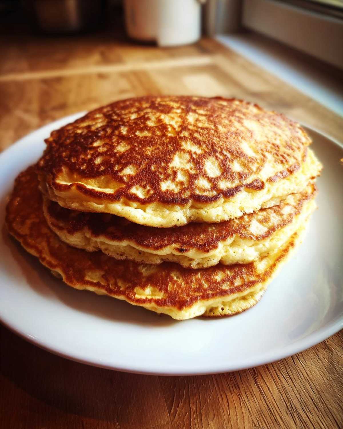 A tall stack of three golden brown, fluffy almond flour pancakes served on a white plate.