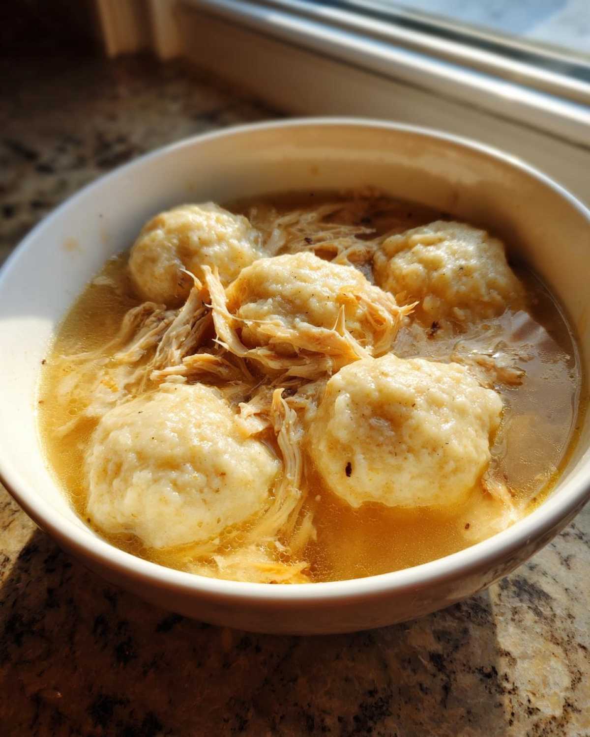 A close-up of fluffy chicken and dumpling soup, featuring tender shredded chicken in broth with four large dumplings.