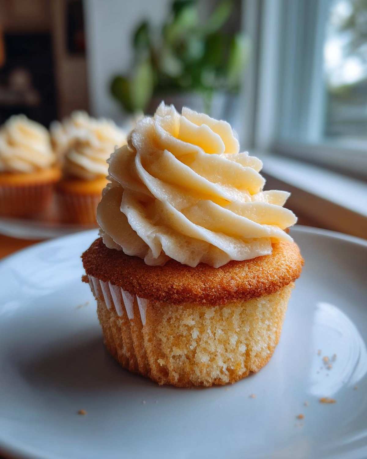 Close-up of a single, fluffy vanilla cupcakes topped with a high swirl of pale yellow buttercream frosting.
