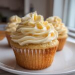 Close-up of a fluffy vanilla cupcake topped with a swirl of pale yellow vanilla buttercream frosting.