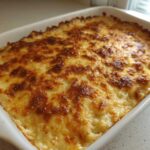 A white baking dish filled with golden brown, bubbly french onion butter rice casserole.