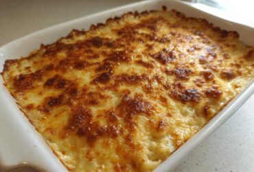 A white baking dish filled with golden brown, bubbly french onion butter rice casserole.