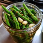Close-up of bright green dilly beans packed tightly in a glass jar with garlic cloves and pickling spices.
