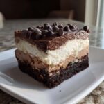 A decadent slice of brownie refrigerator cake showing a dark brownie base, two creamy mousse layers, and chocolate chips on top.