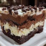 Close-up of a rich slice of brownie refrigerator cake showing layers of brownie, cream, and chocolate mousse topped with chips.