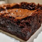 Extreme close-up of a thick, fudgy brownies square showing its dense texture and shiny, crackled top.
