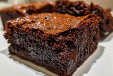 Extreme close-up of a thick, fudgy brownies square showing its dense texture and shiny, crackled top.