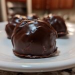 A close-up of several rich, dark chocolate-coated Oreo balls resting on a white plate.