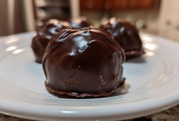 A close-up of several rich, dark chocolate-coated Oreo balls resting on a white plate.