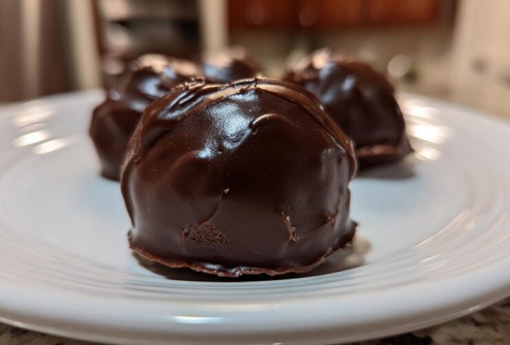 A close-up of several rich, dark chocolate-coated Oreo balls resting on a white plate.