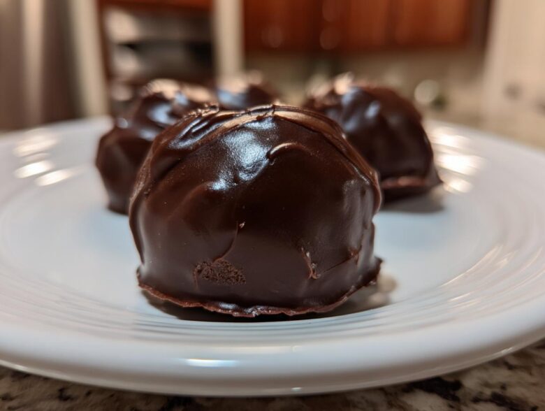 A close-up of several rich, dark chocolate-coated Oreo balls resting on a white plate.