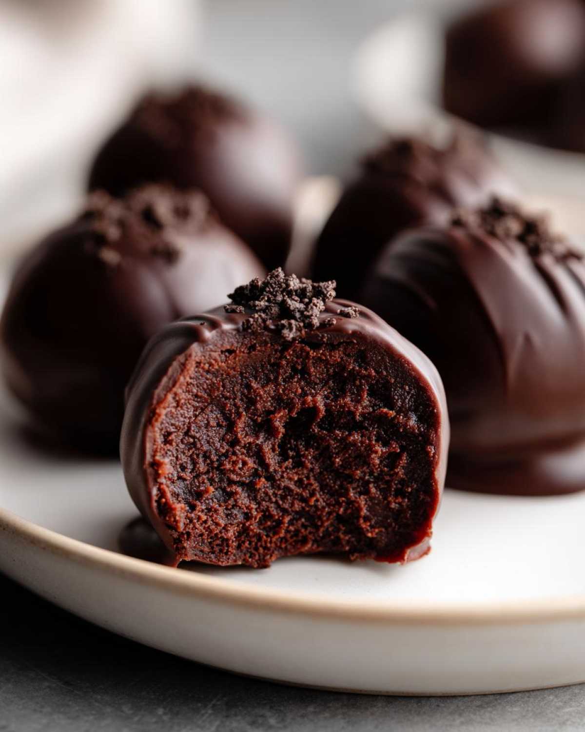 Close-up of a chocolate-dipped Oreo ball with a bite taken out, revealing the fudgy interior and cookie crumb topping.