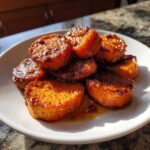 A stack of thick, round slices of candied yams glistening with a rich, dark glaze, served on a white plate.