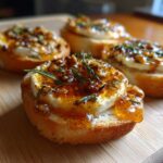 Close-up of one of the amazing goat cheese and honey bites on toasted baguette slices, topped with honey glaze and rosemary.