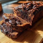 A dark, rich loaf of hot fudge brownie bread with two slices cut, sitting on a wooden cutting board.