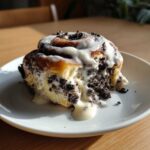 A single, gooey Oreo cinnamon rolls slice covered in white icing and crushed cookie pieces.