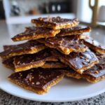 A stack of broken pieces of homemade graham cracker toffee snap layered on a white plate.