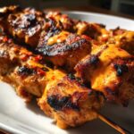 Close-up of grilled bang bang chicken skewers drizzled with spicy orange sauce and red pepper flakes.