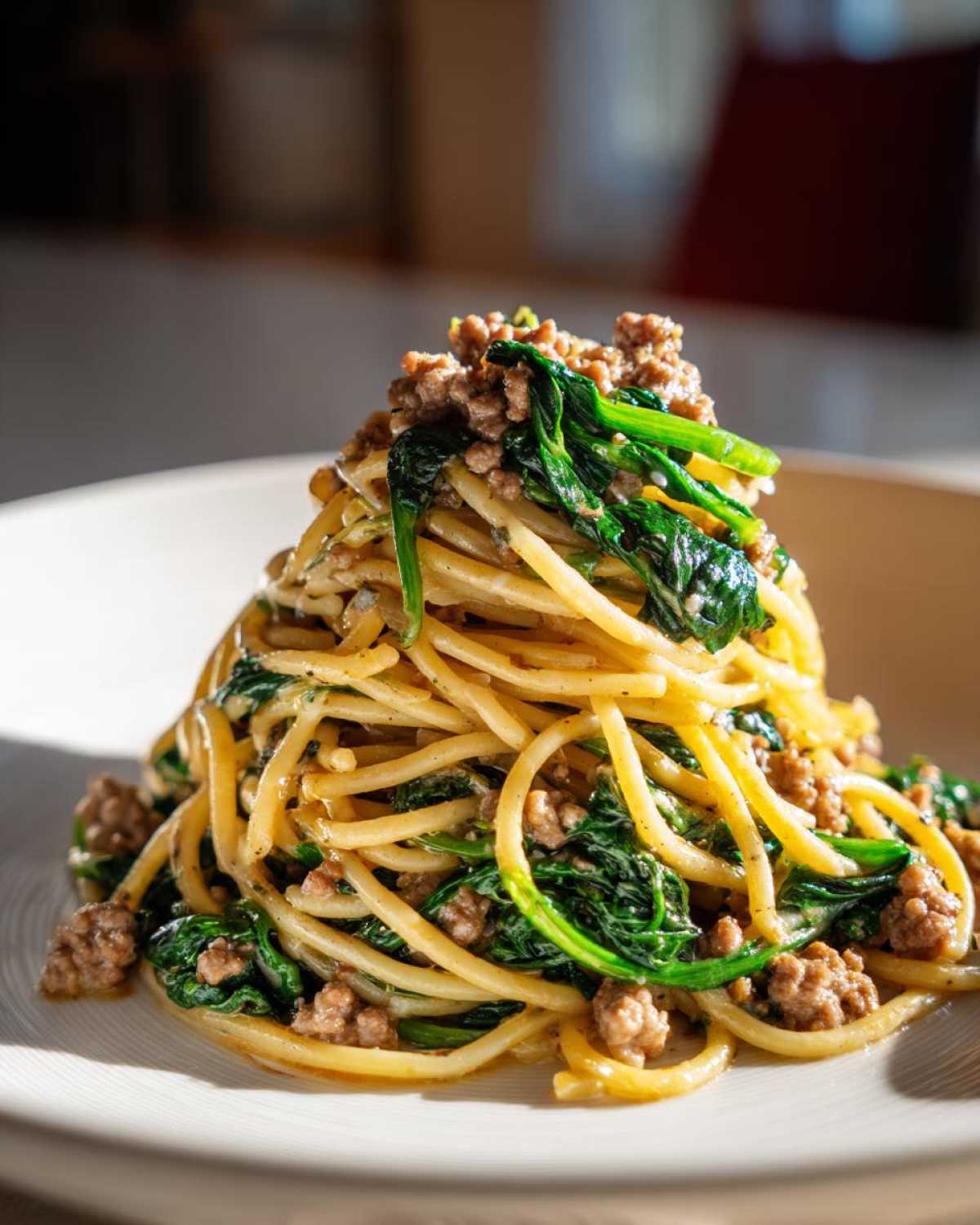A tall mound of spaghetti tossed with ground turkey pasta sauce and wilted spinach on a white plate.