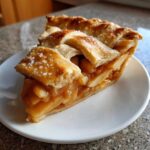 A close-up of a thick slice of homemade apple pie featuring a golden lattice crust sprinkled with sugar.