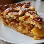 Close-up of a perfect slice of homemade apple pie showing caramelized apples and a flaky, sugared lattice crust.