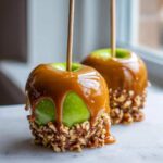Close-up of a glossy green caramel apple dipped in thick caramel sauce and rolled in chopped nuts.