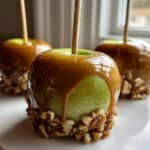 Close-up of a glossy, dripping caramel apple dipped in chopped nuts, ready to eat.