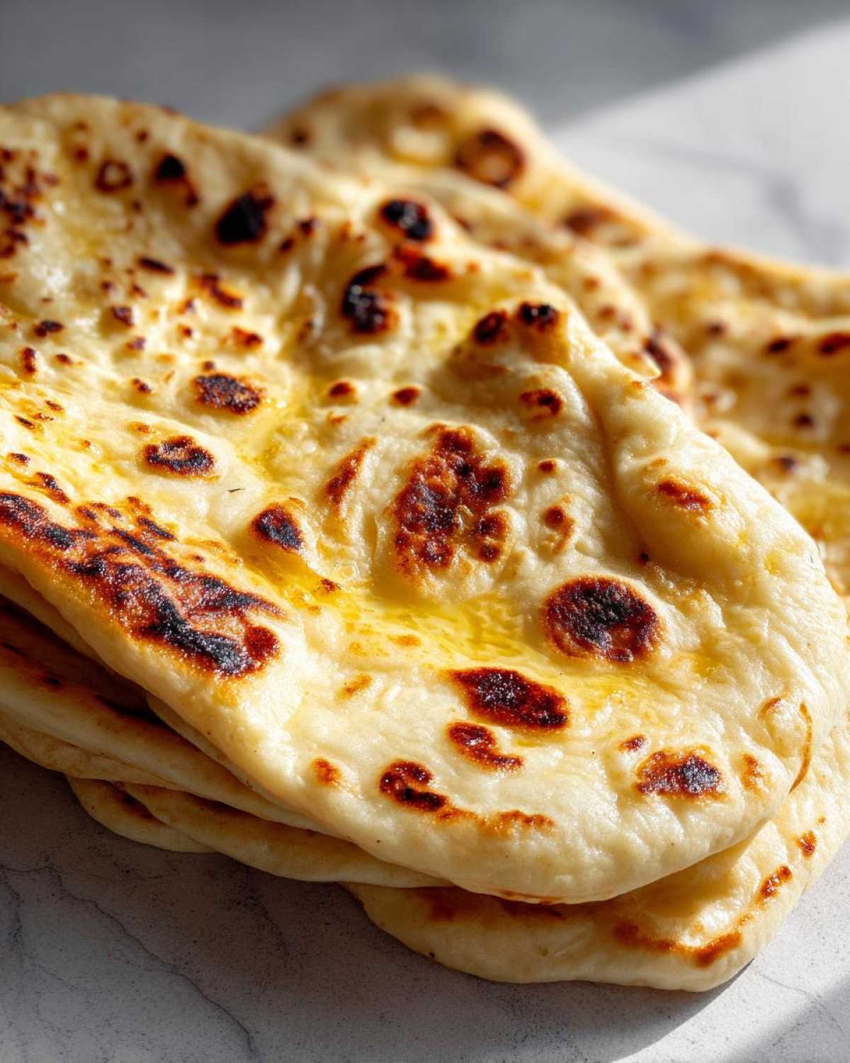 Close-up of a stack of soft, fluffy homemade naan bread brushed with melted butter and showing charred bubbles.