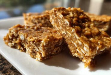 Close-up of several chewy, homemade protein bars made with oats, sitting on a white rectangular plate.