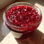 Close-up view of vibrant, glistening homemade raspberry jam filled to the top of a glass jar.