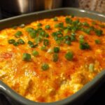 Close-up of a bubbling hot buffalo chicken dip topped with melted orange cheddar cheese and chopped green onions.