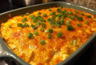 Close-up of a bubbling hot buffalo chicken dip topped with melted orange cheddar cheese and chopped green onions.