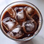 Overhead view of a glass filled with rich, dark chocolate milk and large ice cubes, perfect for iced chocolate milk.